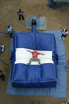 Gliding fast between buildings, Batman works his way to the landing spot, illuminated by an LED bat atop a nearby rooftop. He smacks down onto a large stunt airbag, the glider is damaged, but Bruce is not. Alfred helps him off the bag and the two quickly disassemble the gear.