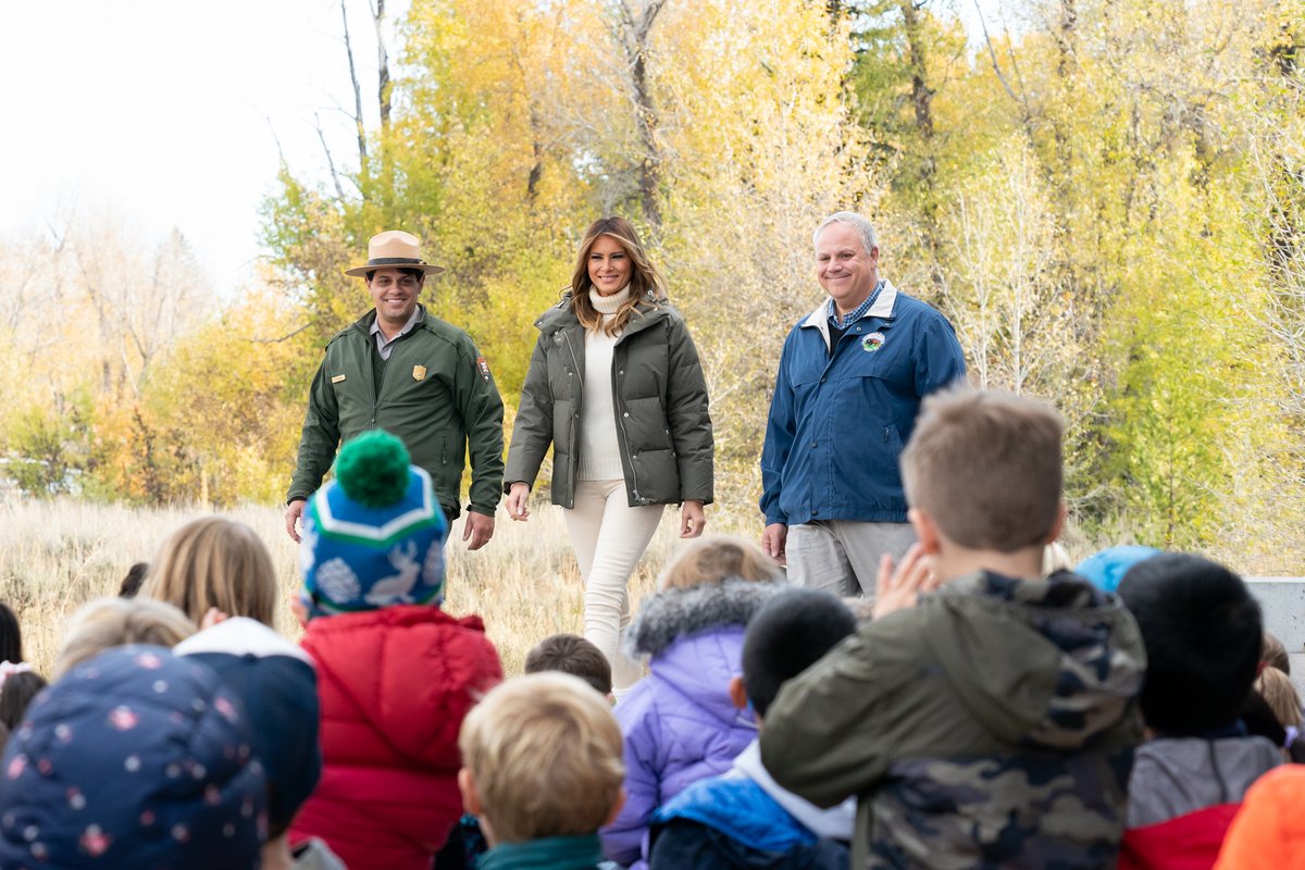 An NPS employee in uniform with Melania Trump and David Bernhardt stand before a group of children in a park.