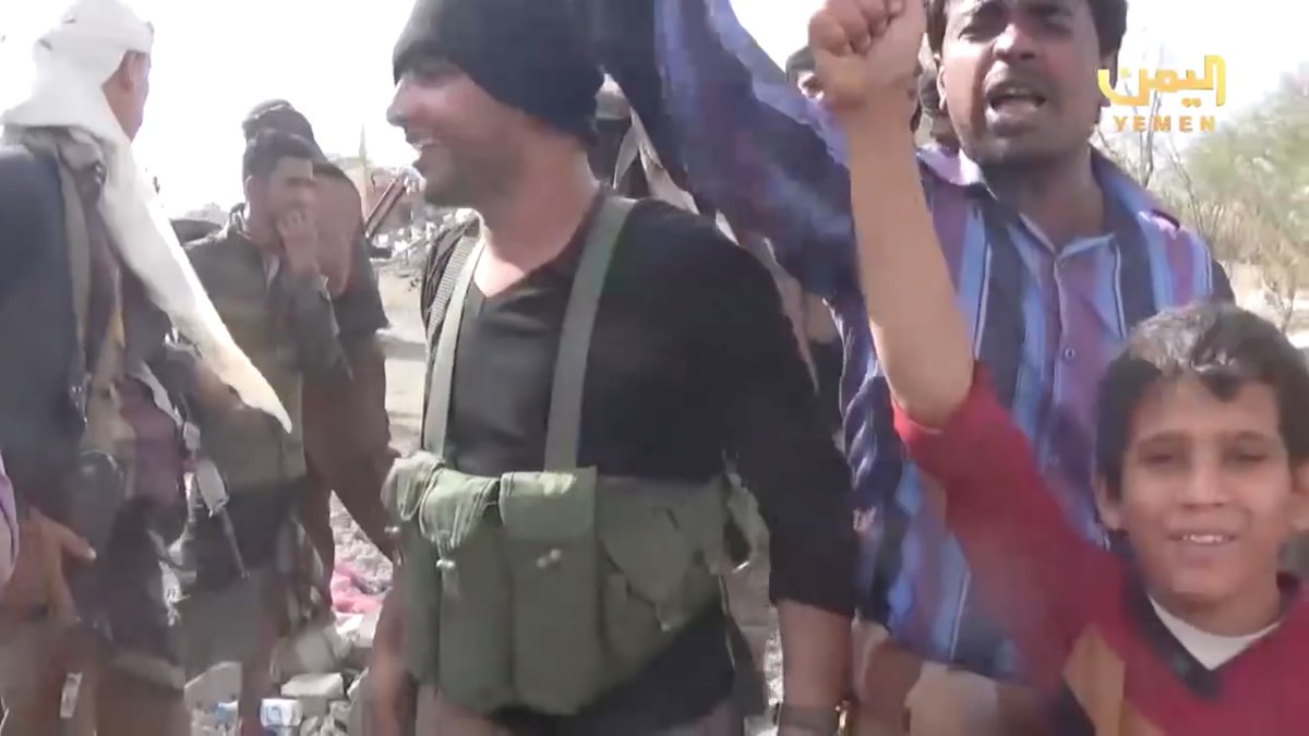 Among the celebrating militiamen were quiet men who resolutely looked away from the camera or covered their faces.Look at the tall, skinny guy on the left, and then the man in the background drinking from a plastic bottle.