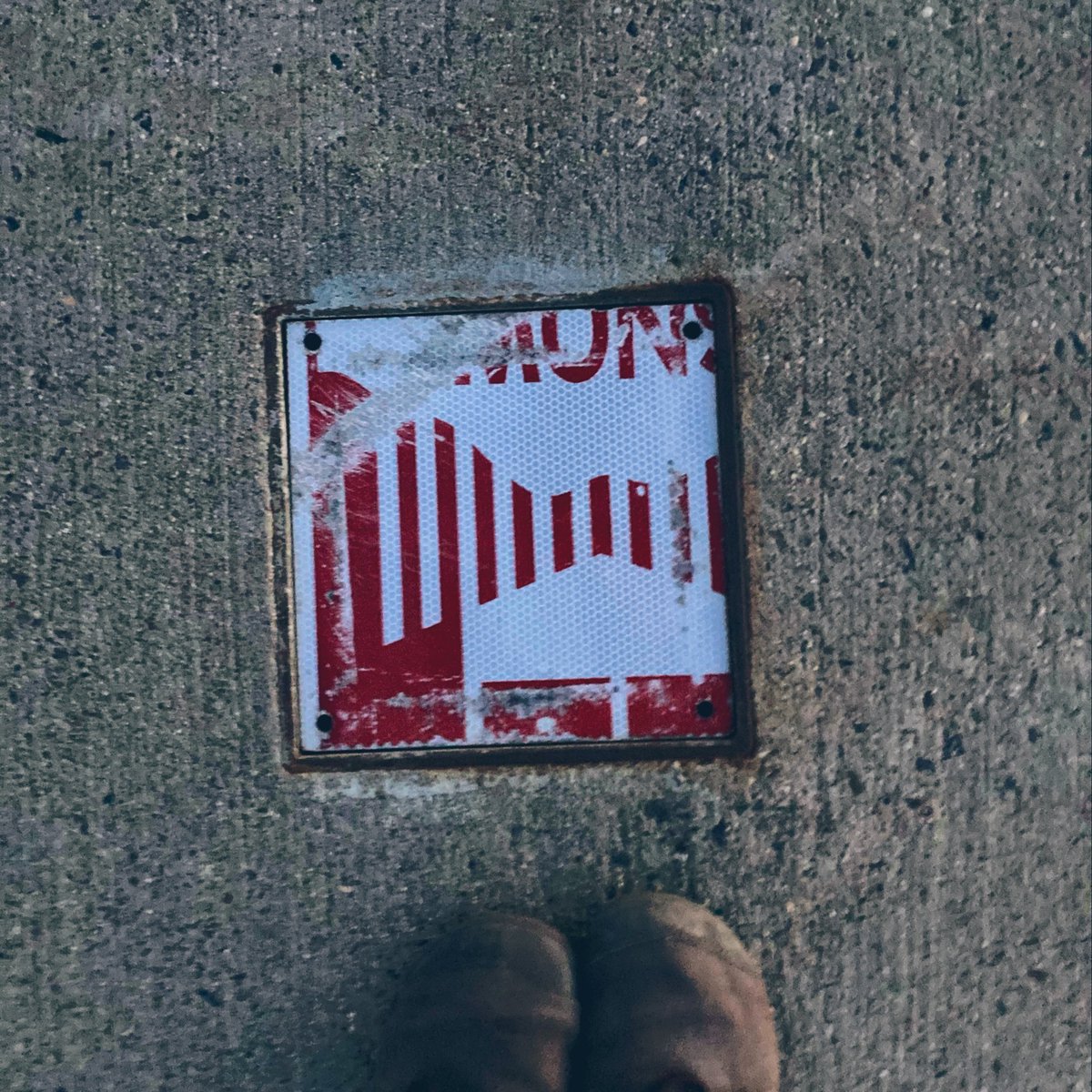 An old snow emergency sign cut to fill a hole in the concrete on a pedestrian bridge.