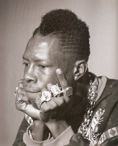 the one-sleeved top over the purple sweater, the big gold rings and glasses. >>>