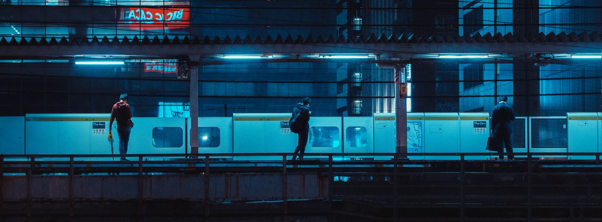 Photography by Liam Wong of Tokyo at night. A train station platform captured four times. This image is of three men spaced equally apart waiting for the next train.