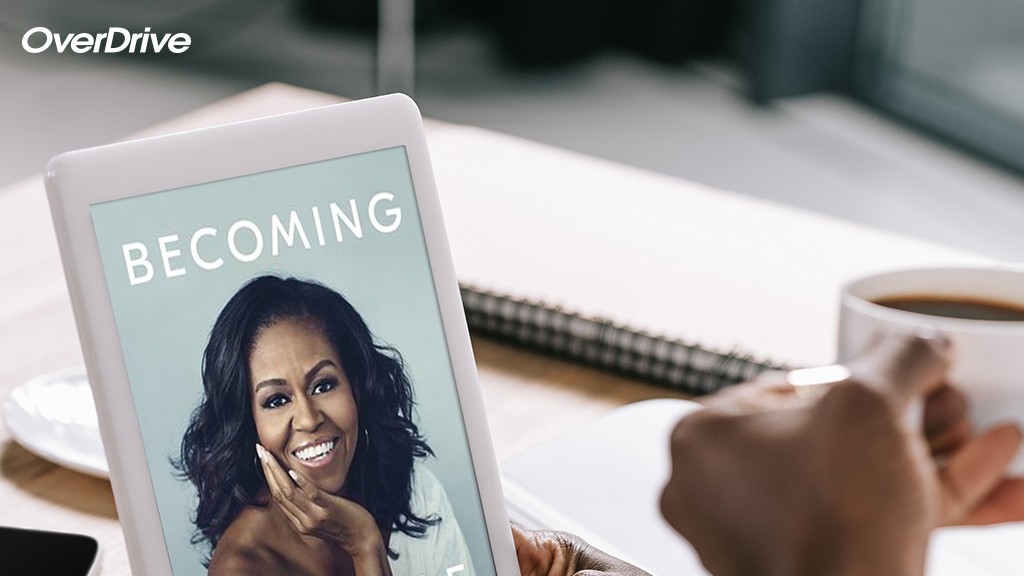 a woman looking at her kindle holding a cup of coffee, the screen featuring Michelle Obama