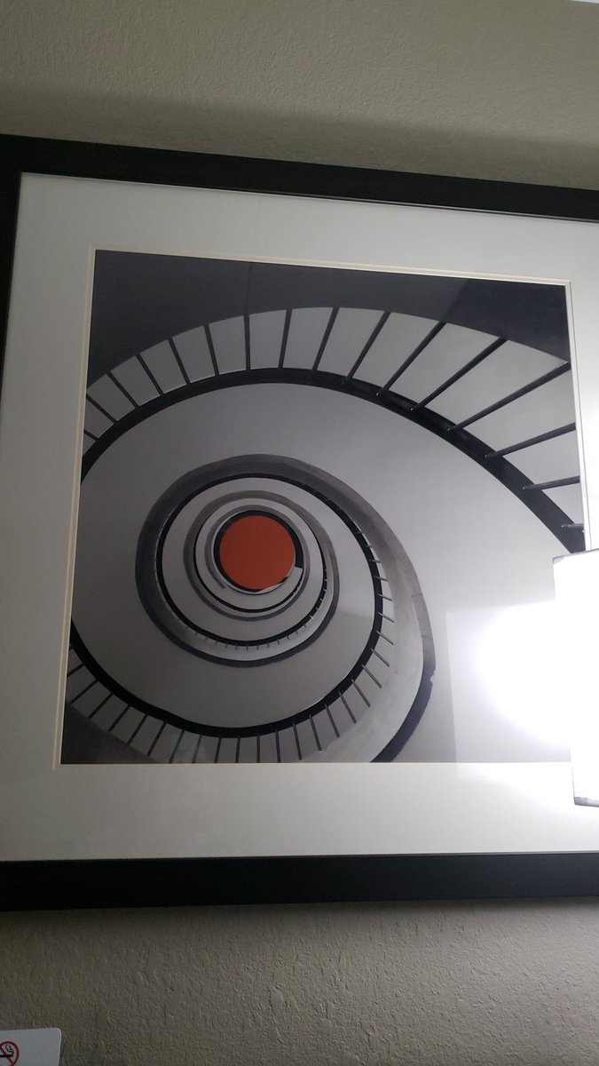 rayleemental's tweet photo. Day 1 of my Hotel Art Review. Des Moines, Iowa. The perspective of the staircase makes me feel like I'm looking towards the sky but the hole at the top(?) of the staircase looks more like a sink drain to me. It leaves me feeling confused. 6/10 https://t.co/x1z60yPqtS