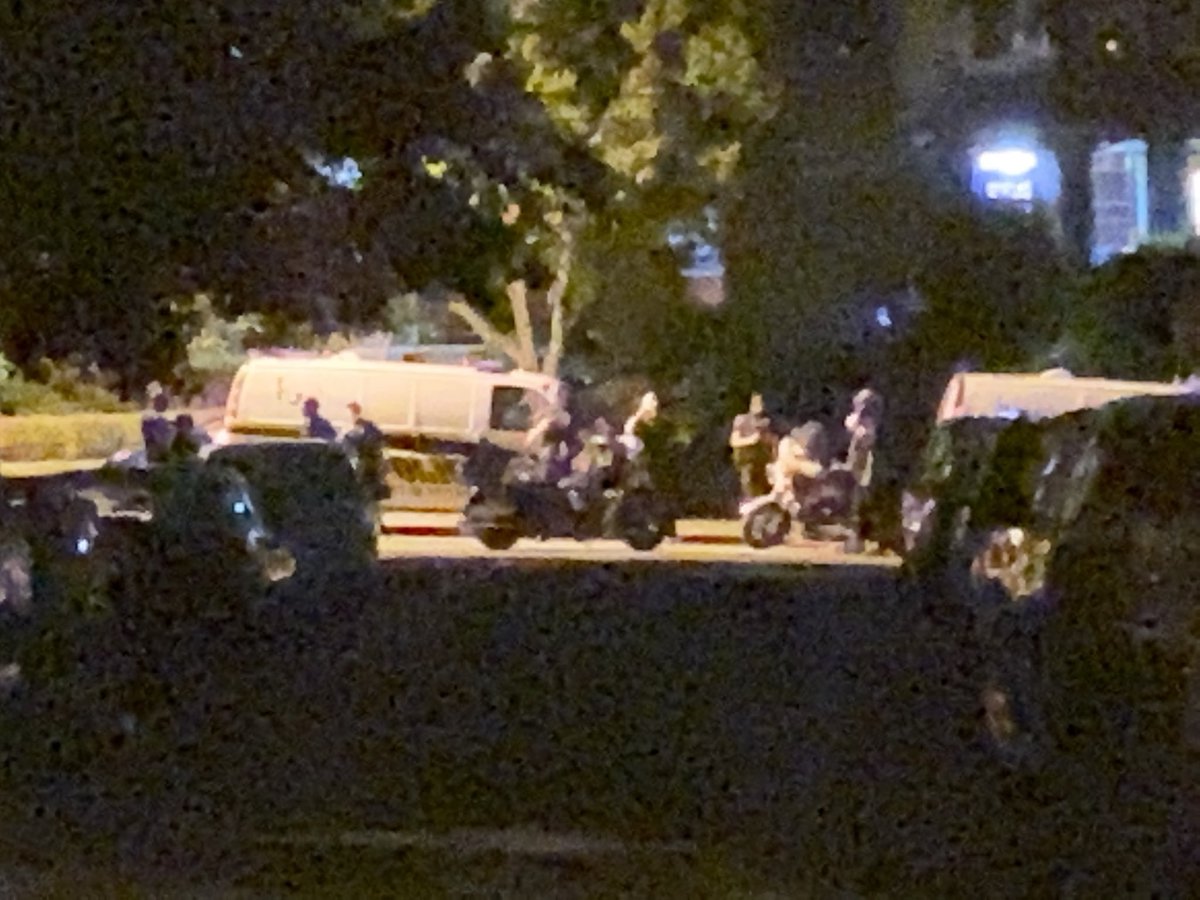 My camera can’t get closer but I see two police vans and a few dozen officers down the street, aggressively shining their light at people on the street.