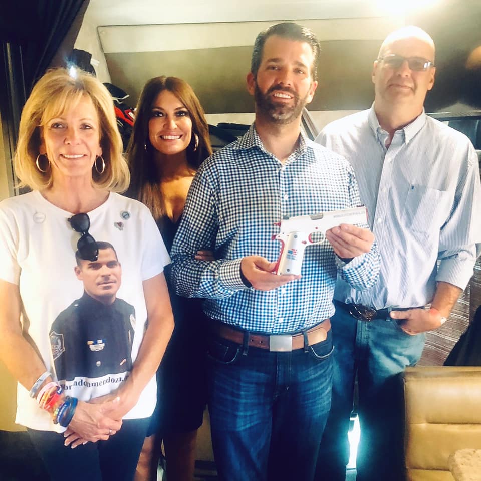 Donald Trump Jr. holding a "We Build The Wall" branded gun while standing with two advisory board members in July 2019.  https://www.facebook.com/WeBuildTheWall/photos/a.314970215820571/407324403251818/