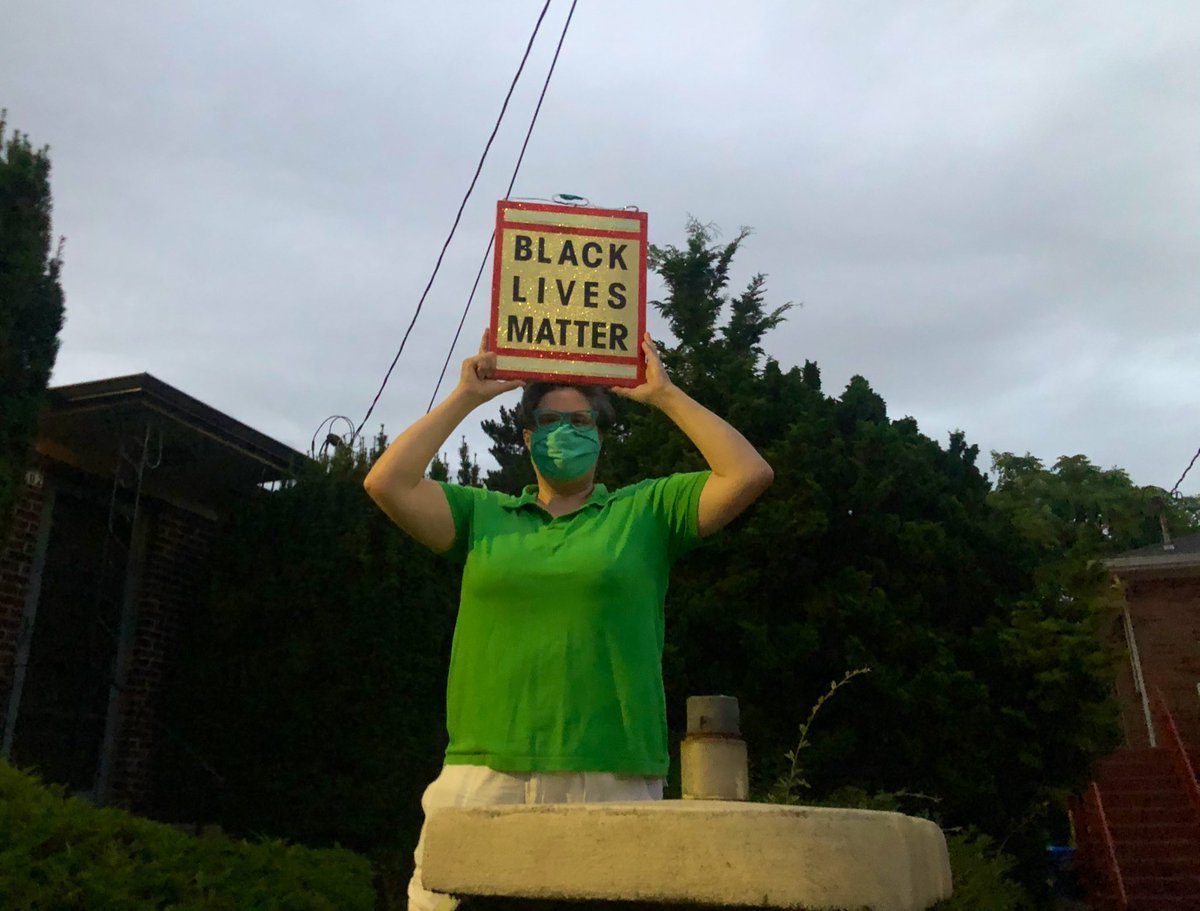 Neighborhood resident comes out in the rain to hold up a sign reading “BLACK LIVES MATTER”