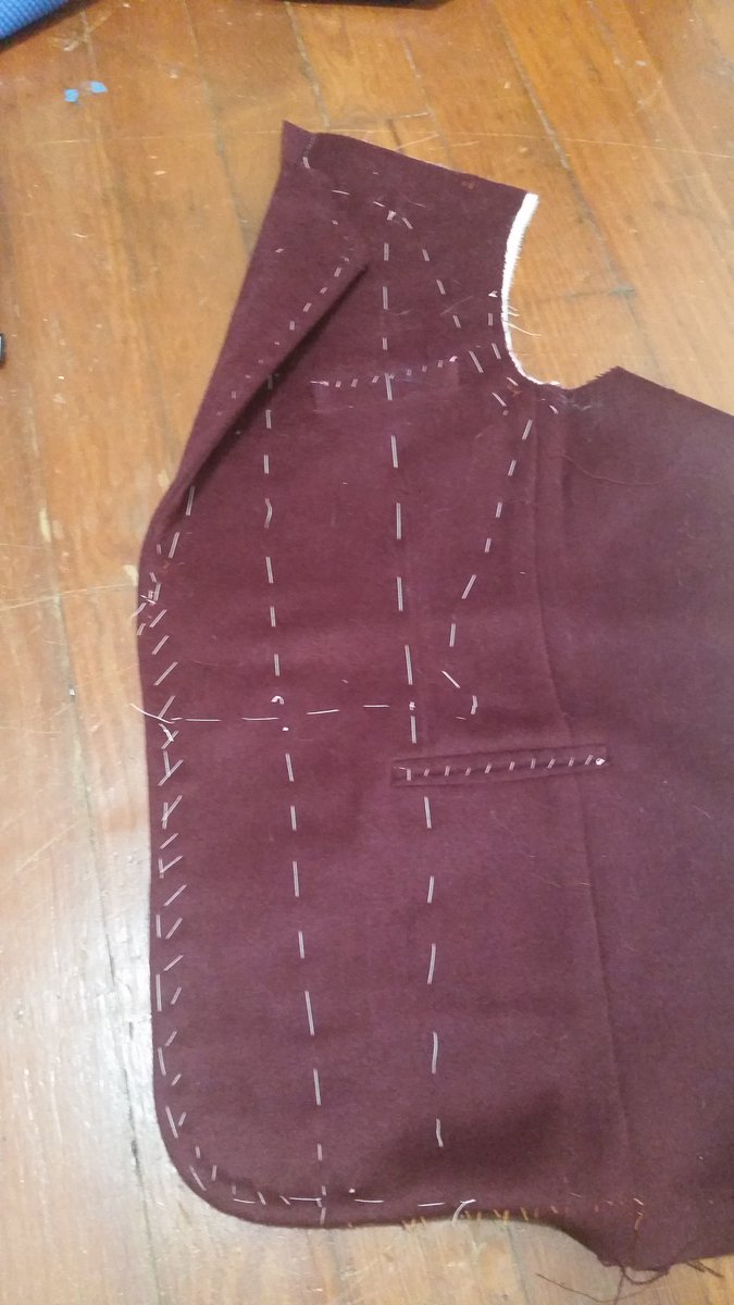 The lapel point and the curved bottom edge are both tacked to the tape, allowing me to control and keep it flat, even on this thick fabric. Then we turn and baste along the edge so the seam edge is turned one way at the lapel, and the other the rest of the way.