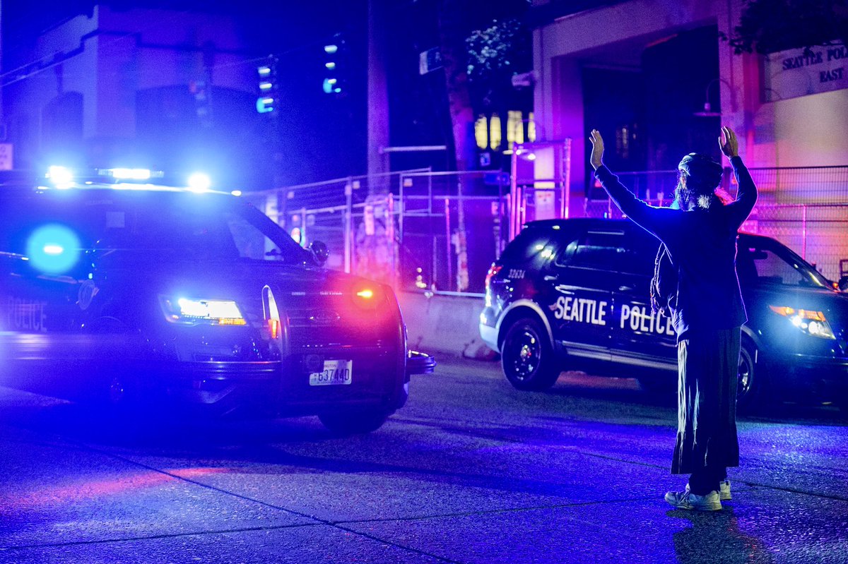 Couple scenes from  #seattleprotests last night at the East Precinct. After a small group of protestors blocked the side entrance to the station, SPD responded with a large force of cars with lights & sirens. SPD retreated after protestors approached them slowly with raised hands.