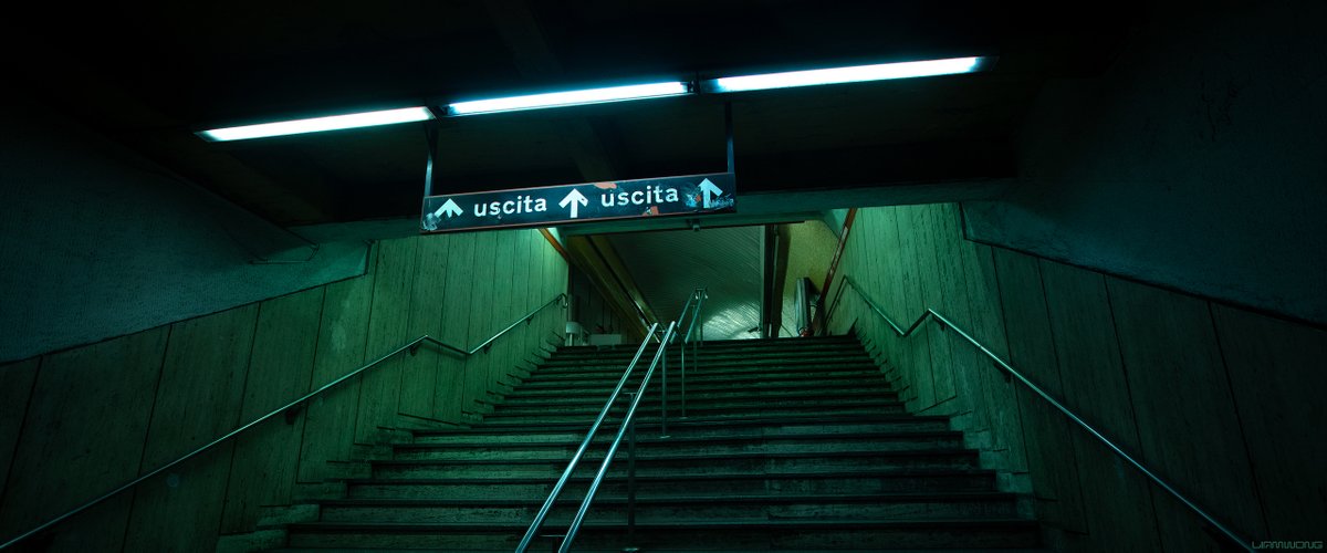 Photography by Liam Wong of subways at night. This image is of Rome's subway station. It has a green tint to it. The signs read 'Uscita' and have arrows pointing upwards.