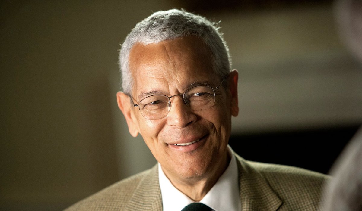 A photo of the late civil rights leader Julian Bond, who is seen wearing a suit and a pair of glasses, and smiling.