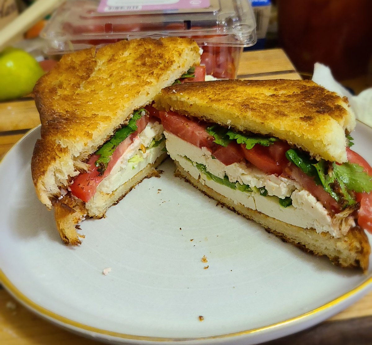 a sandwich sliced in half diagonally with toasted bread, and layers of cheese, tomato, chile pepper, and cilantro inside