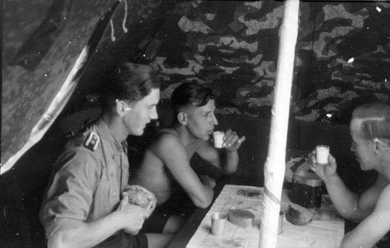 On the face of it a standard picture of guys enjoying a meal in their (at least) 8 man zeltbahn. See the field made pole (2 in an 8 man). A 4 man could not enable that ‘roomy’ pic. The interesting detail is the use of both Heer/LW splinter & WSS camo in this instance. 21)