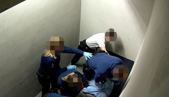 When Jozef doesn’t stop hitting his head against the wall, a few policemen cuff his hands and ankles. Five police agents were kneeling down on him, a sixth agent has to check his face. 5/9