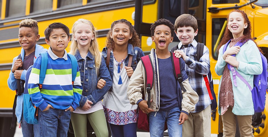 a group of seven children standing in front of a schoolbus