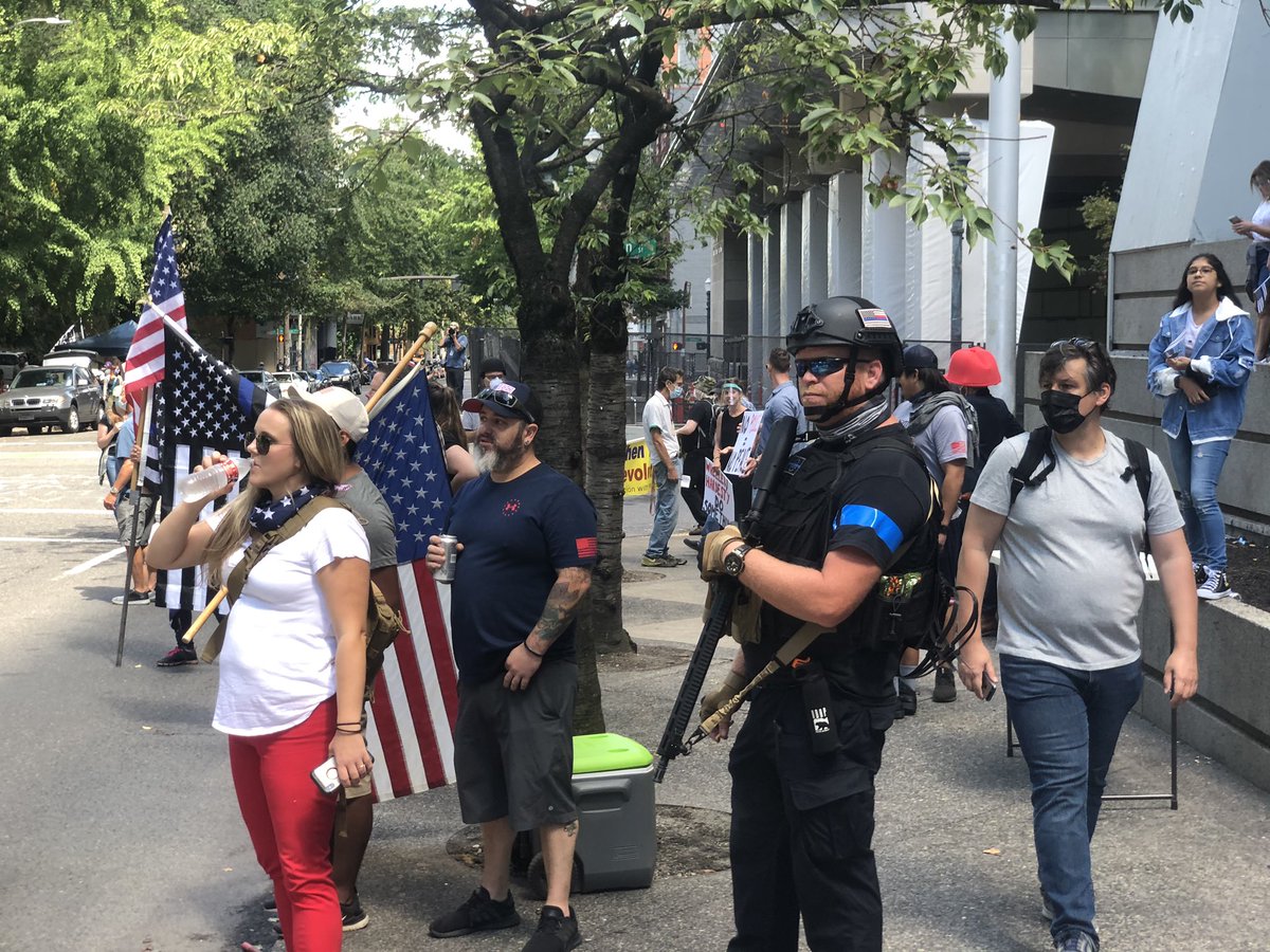 Guy with rifle and III% patch standing with the pro police/pro Trump group.