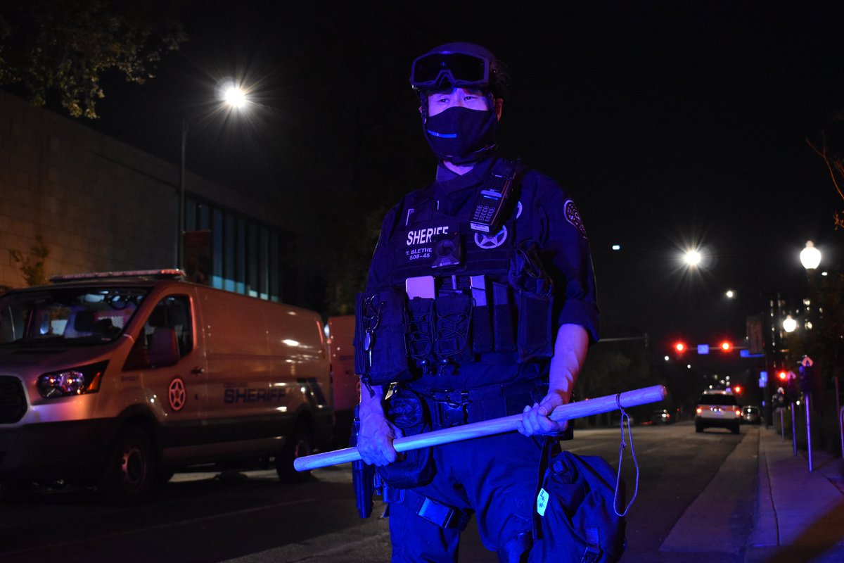 TroutBoneless's tweet image. Officer Blethe wields a large wooden stick with a rope fixed to the end. Uncertain what purpose this stick serves. #DPDActivity #DenverProtests #DefundThePolice