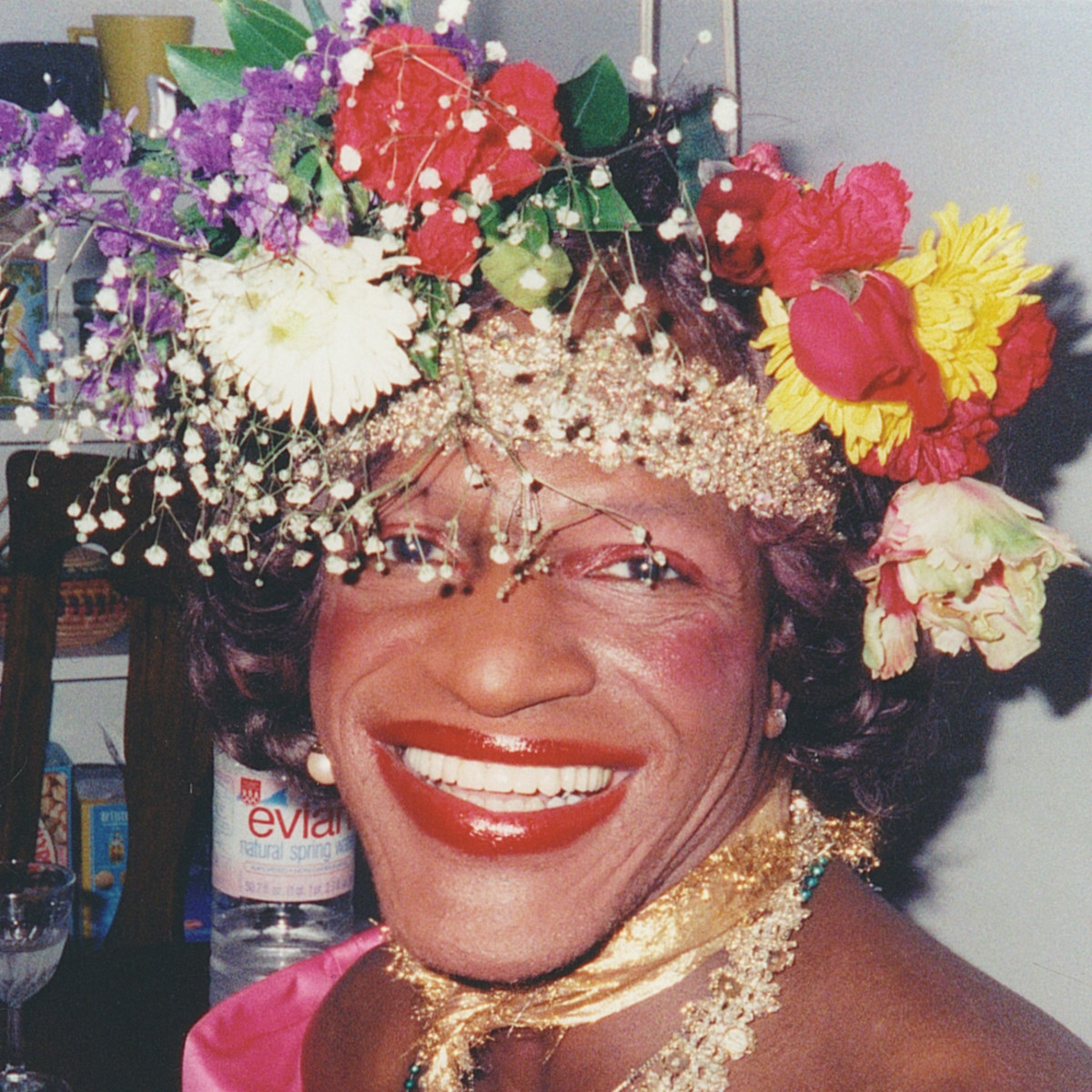 A photo of Marsha P. Johnson smiling and wearing a colorful headpiece adorned with flowers.