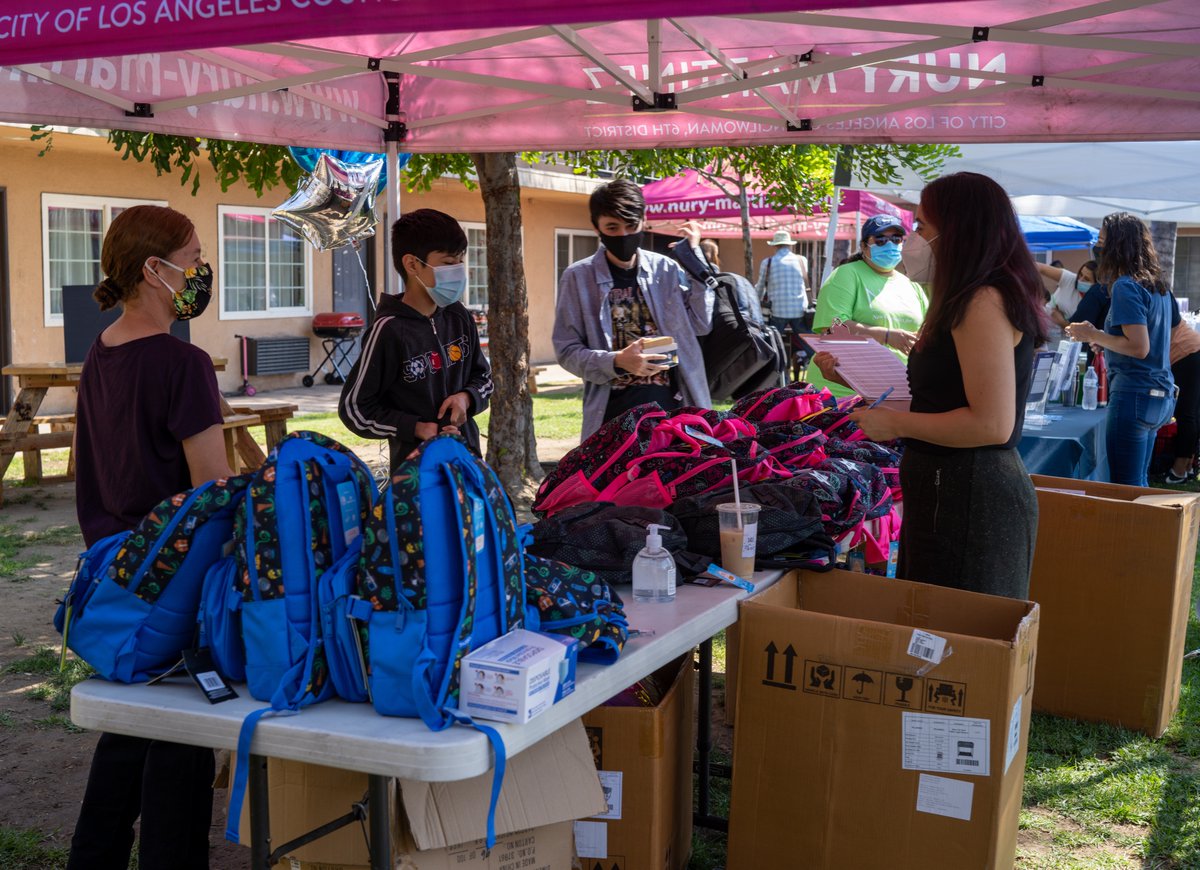 Three people looking at backpacks and a person with with a clipboard behind the table.