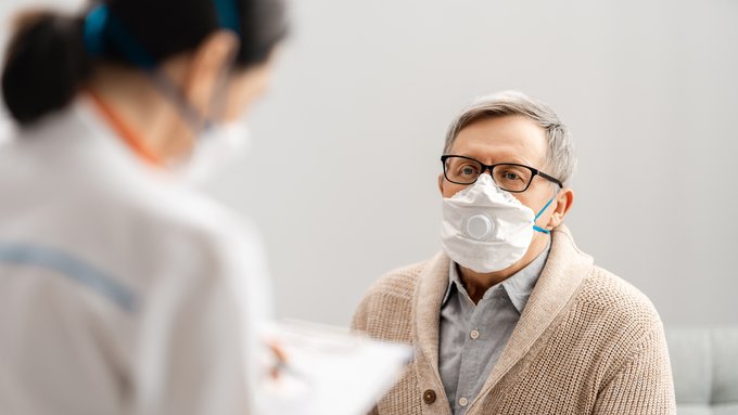 Imagen: Una doctora y un paciente con mascarillas hablan sobre asuntos de salud.