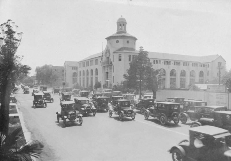 Cars driving down the street with building in the background.