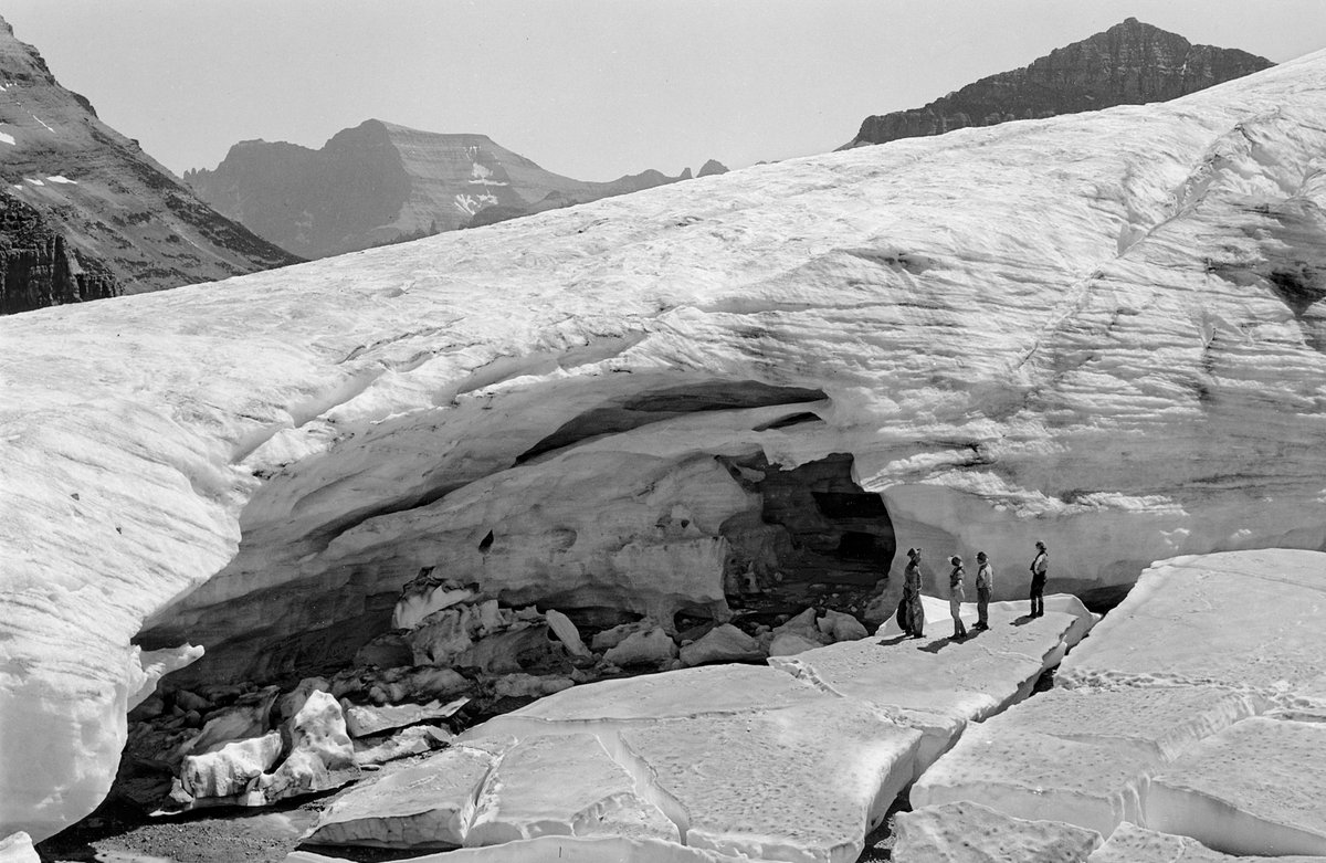 In 1932, many visitors saw Glacier National Park by horseback. One multi-day trip took clients along the north face of Boulder Peak, where they encountered Boulder Glacier. At the time (as seen in the first photo), a cavernous entrance into Boulder Glacier dwarfed the 4 onlookers