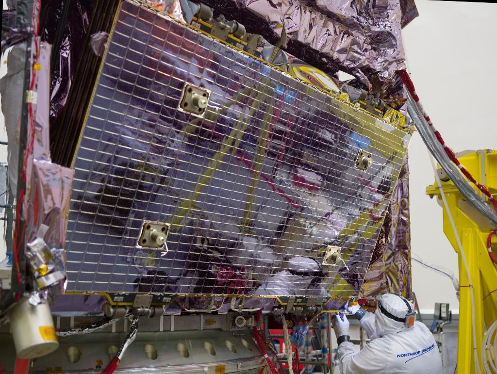The reflection of a technologist can be seen on a folded panel as they work to install the solar array onto the Webb telescope.