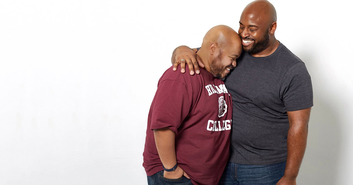 Two men embracing in front of a white background