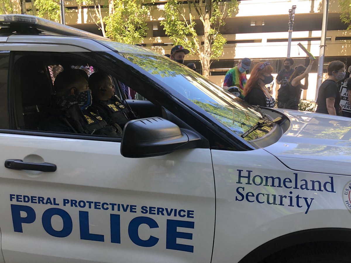 Inside the Homeland Security/Federal Protective Service police vehicle, one officer wears a thin blue line mask. The other officer isn’t wearing a mask.