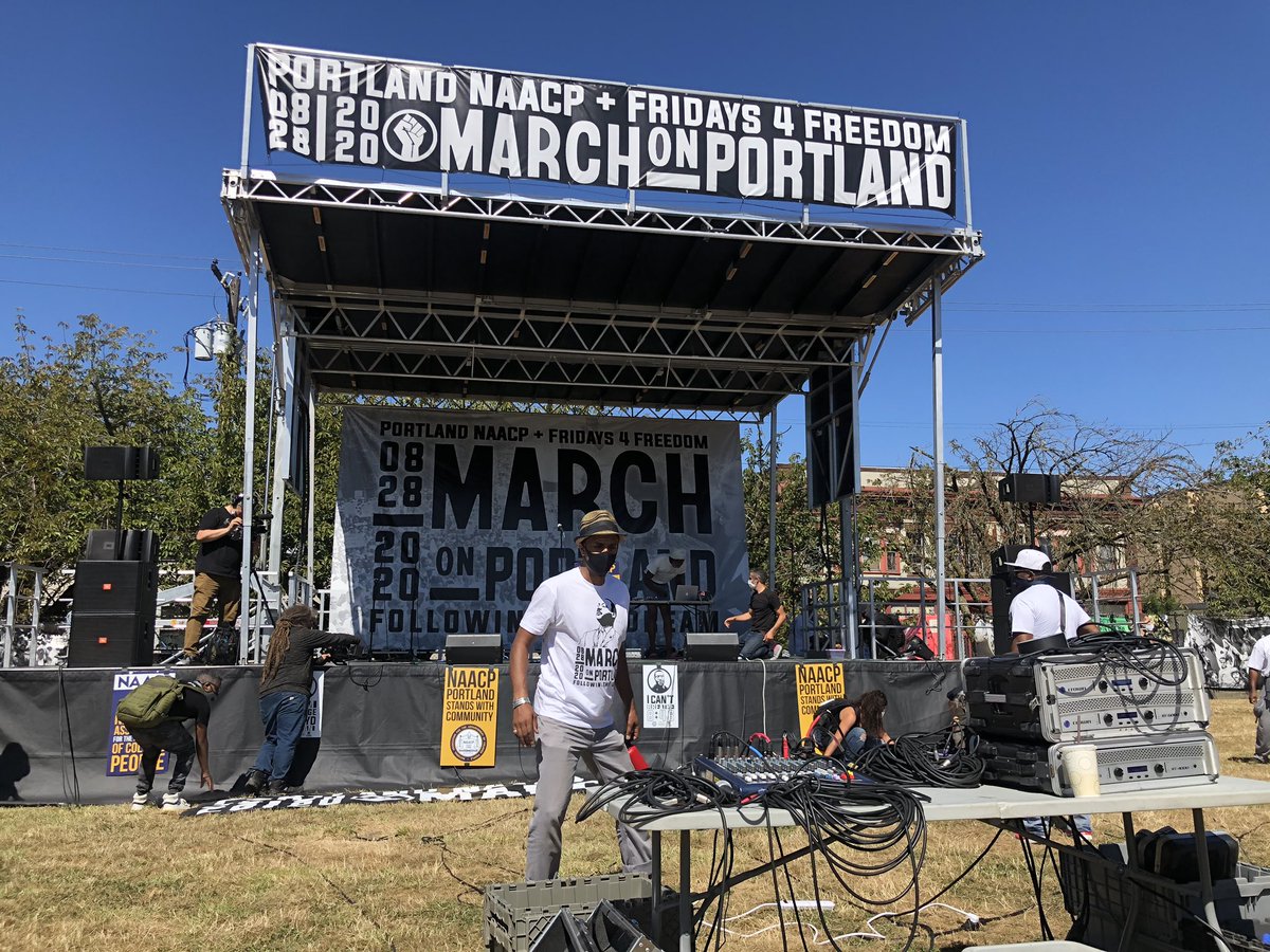 As the crowd fills the park outside Revolution Hall, they’re met with free pizza, hand sanitizer and a concert stage. Flowers, banners and photos of Black victims of police killings are threaded through the park’s fences.