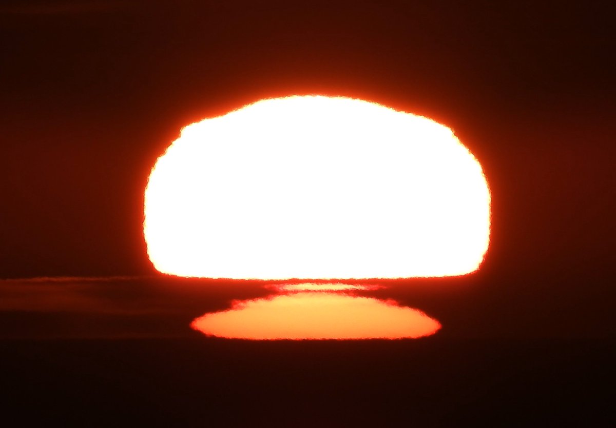 Thankfully this was not what it appears to be! Before reaching the horizon, the Sun started moving behind an inversion layer in the atmosphere, where warm air lay over cold air. This causes a mirror image -a 2nd image of part of the Sun under the main disk, but upside down.(4/10)