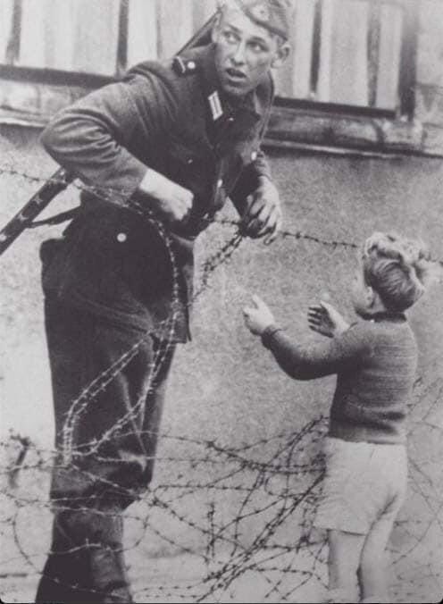 Un soldat allemand aidant un garçon à franchir la barrière pour rejoindre sa famille après la chute du mur de Berlin.