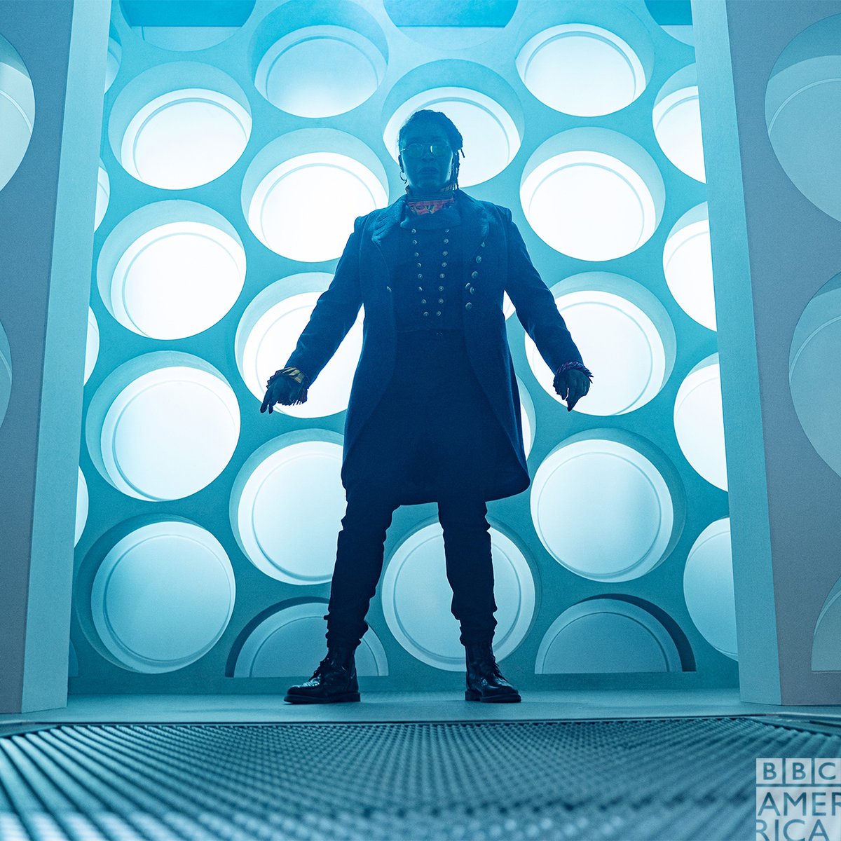 The Doctor standing in front of a blue TARDIS wall covered in the round things