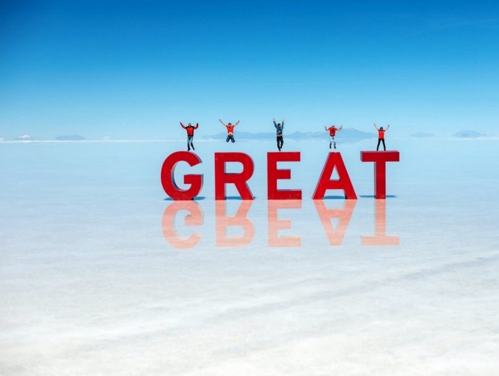 Red-letter blocks saying GREAT in the middle of a salt lake with five people jumping above the letters.