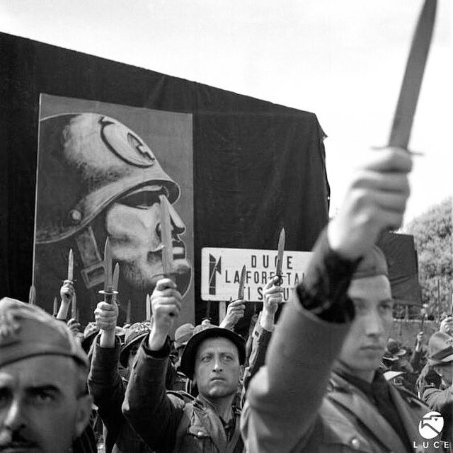 Italian soldiers in Liguria, 1940, raising their daggers in salute, with a portrait of Mussolini behind them. The dagger salute was common in Fascist Italy. The caption reads: “Duce, the Forestale salutes you” (the Forestale was the Italian State Forestry Corps)