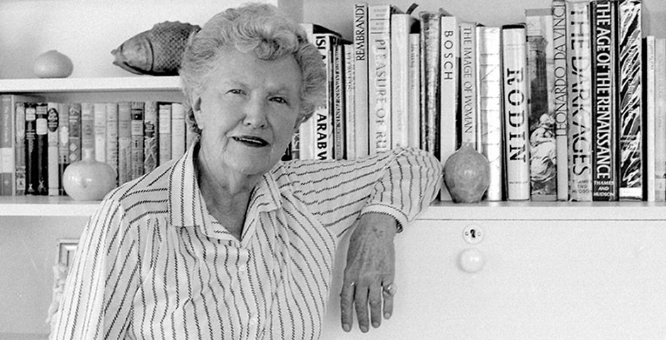 black and white photo of Mary Renault posing in front of a bookshelf full of books