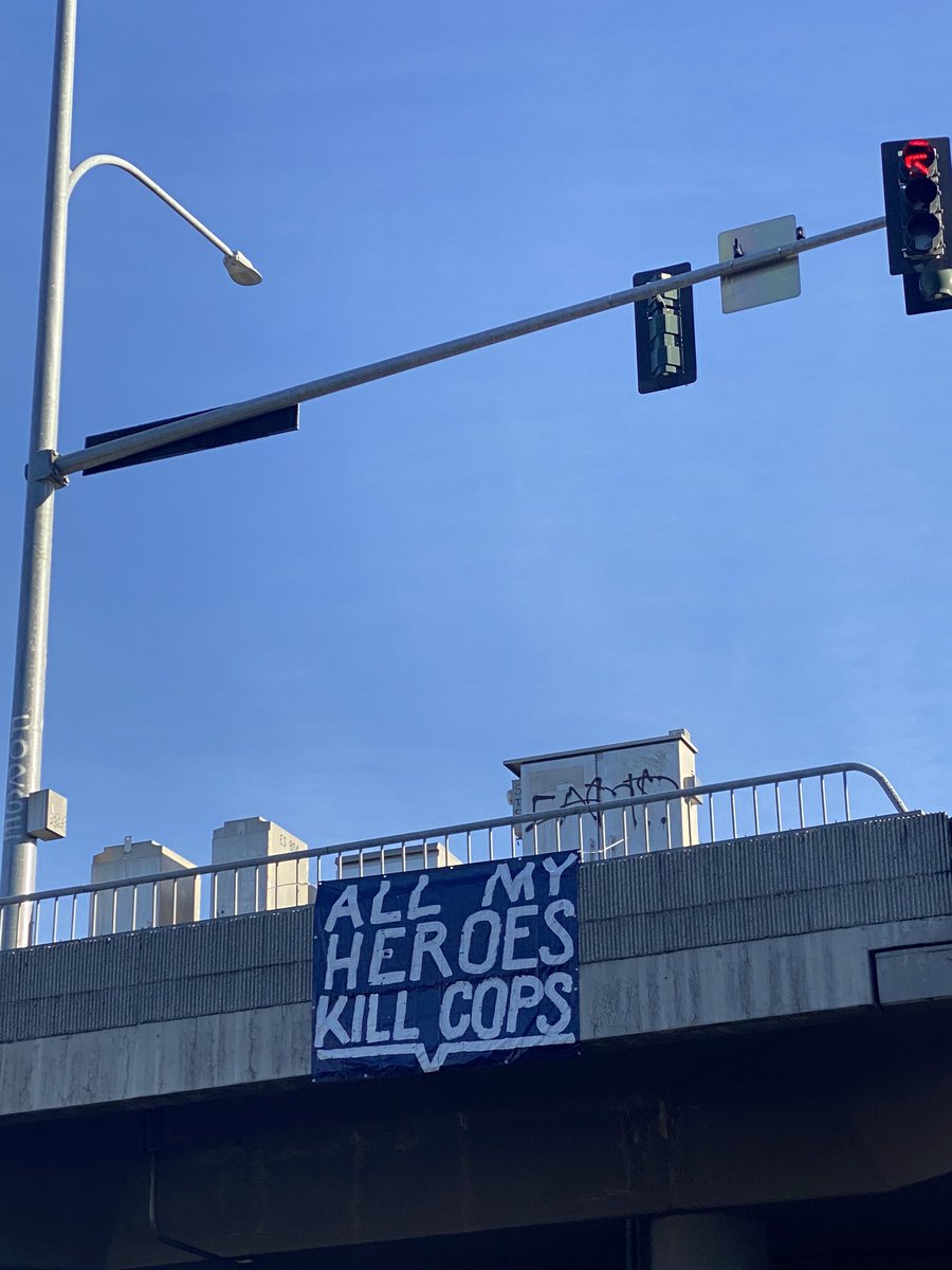 Sign that says “All My Heroes Kill Cops” hangs over the railing as protesters march below.