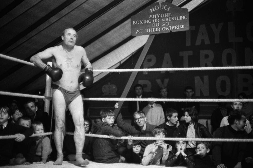 Gloucestershire, 1970.At a village annual summer fête, a man from the audience wearing only his underpants chances his luck, though as the sign says ‘Anyone Boxing Or Wrestling Do So At Their Own Risk.Photo  @HomerSykes