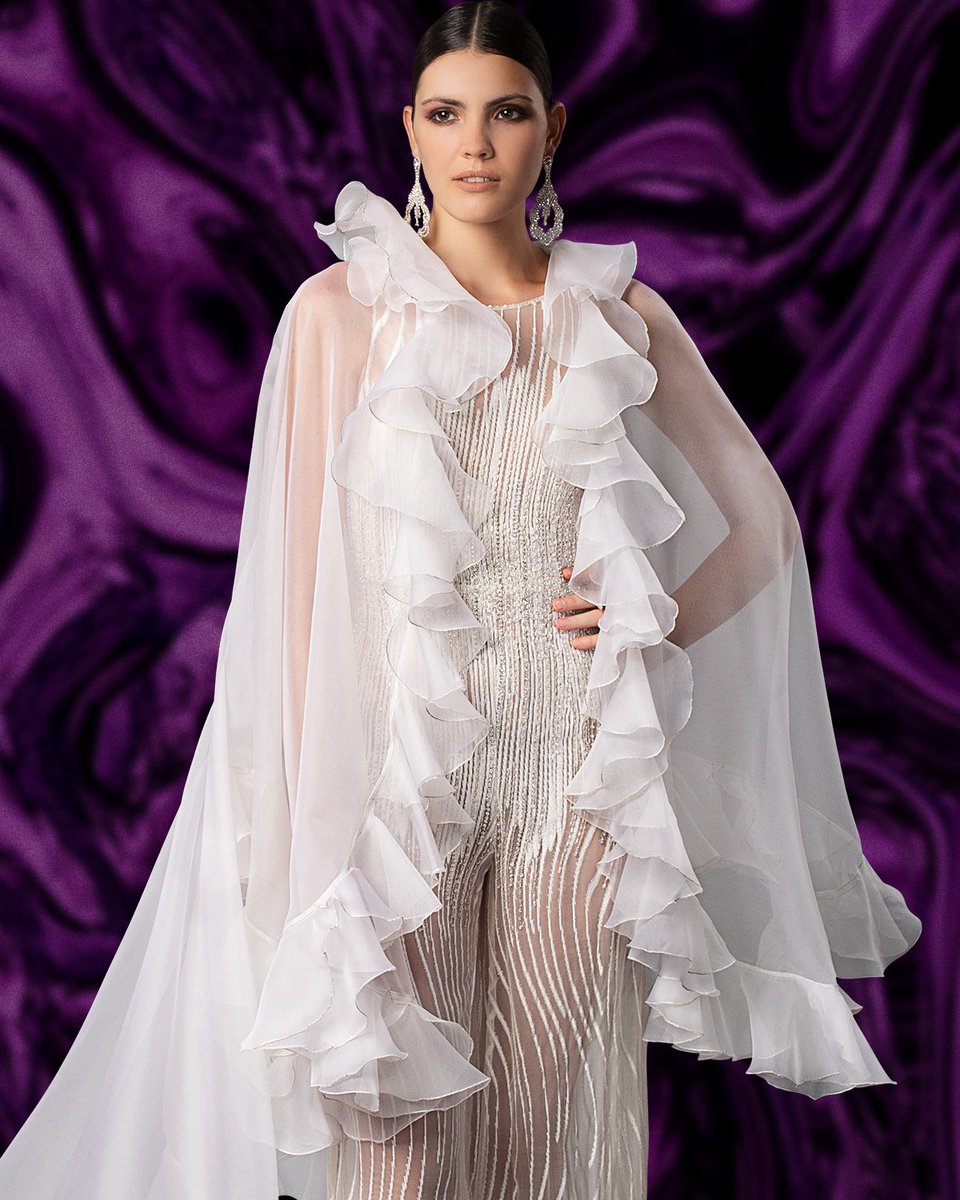 Jumpsuit en tono blanco tiza, realizado en gasa de seda natural con incrustación de nervaduras en chifón, con sugerente transparencia que exalta la figura femenina. Capa en organza de seda con terminación de volantes ribeteados en hilo de lurex plata + en instagram.com/p/CExYyFtJPNu/