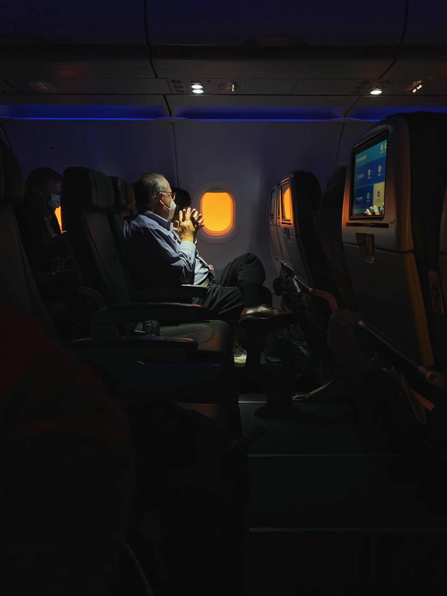 Man wearing a mask looking out a plane window at a bright orange sky