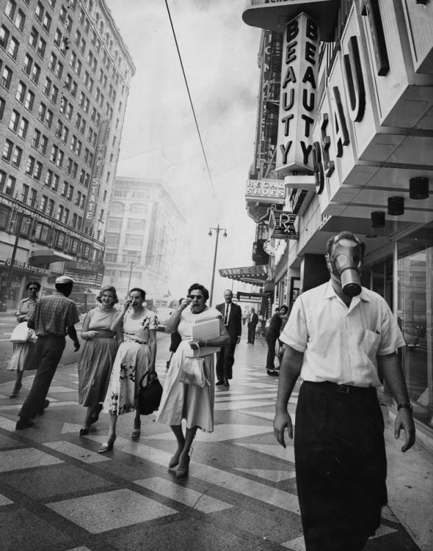 Man Walking down street with gas mask on. Women in back are wiping their eyes.