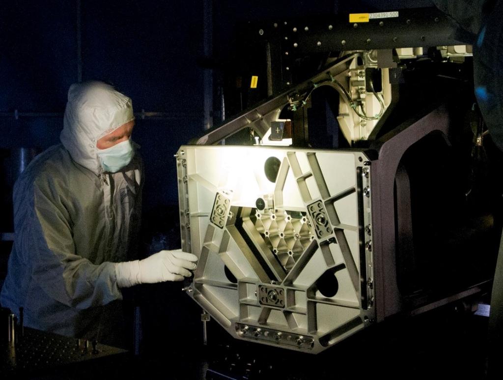 Darvin Muñoz in a cleanroom suit, standing to the left of Webb technology