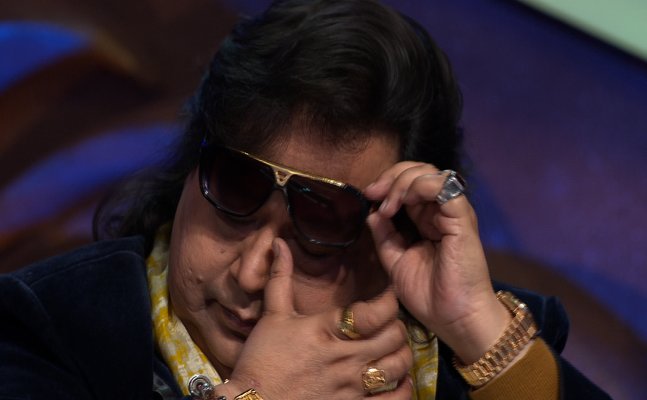 A wall mounted television starts streaming the music video of Addictive, a song by the artist Truth Hurts in which playback artist Lata Mangeshkar is heard singing in the background. The song is Kaliyon Ka Chaman Jab Banta Hai, composed by Bappi Da.