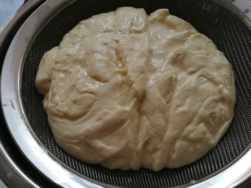 Place the mesh bowl filter on one of your bowls. Using the slotted thingamabob, take the mass of curds out of the pot and place it in the bowl filter, pressing gently as you go to squeeze out the excess whey. It'll look something like this. Almost cheese already.