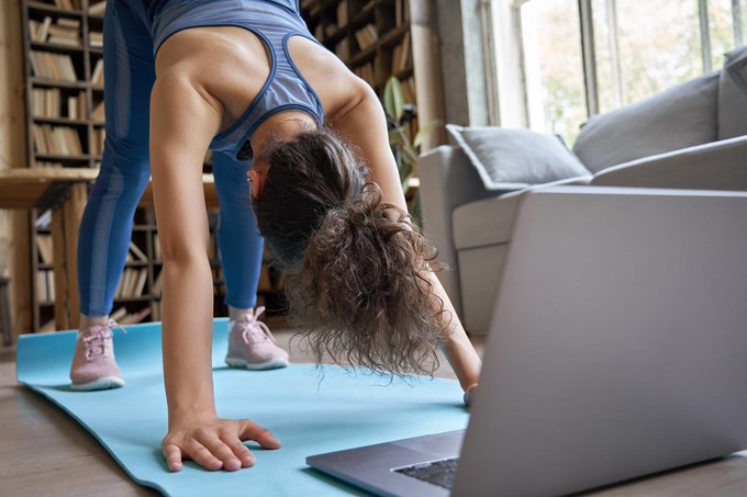 Imagen: Una mujer haciendo ejercicios en la sala de su hogar con una computadora al frente.