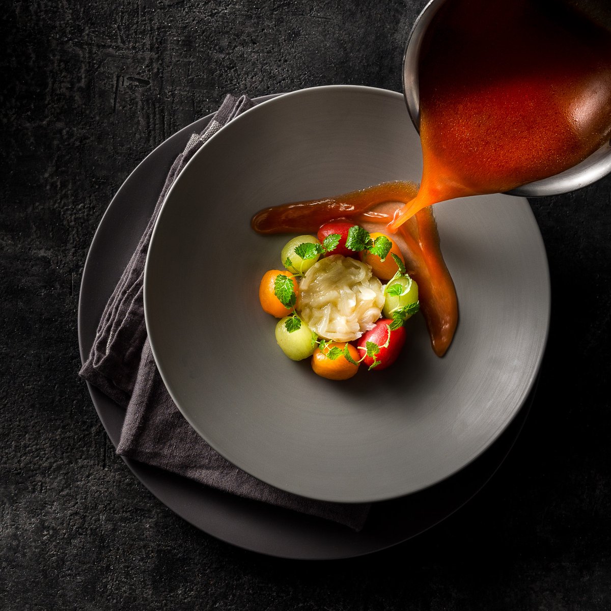 Know Your Onions 🧅 

.

Pouring #tomato broth on a bowl of #vidalia onion stew surrounded by peeled red and yellow grape tomatoes and seedless green grapes. Part of the preparation for Poached Halibut in Modern Greek Cooking by <a href="/chefpano/">Pano Karatassos</a>
