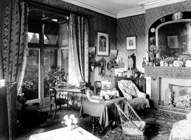 Vamos a ver si nos podemos dar cuenta de algoES 1901Esto es un interior victoriano: Papeles pintados, alfombras y cortinas. Colores oscuros, aspecto desordenado, muchos muebles y objetos de decoración1890 aprox