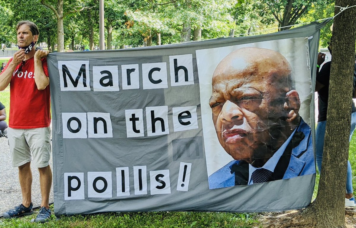 A photo from the 2020 March on Washington in DC, showing a banner that says "March on the polls!" and an image of the late Congressman John Lewis.