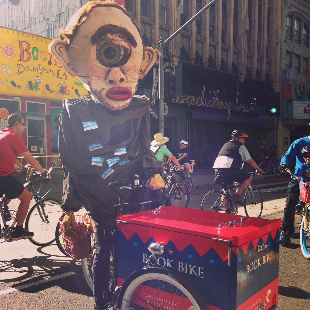 Person in costume with one eye riding the book bike