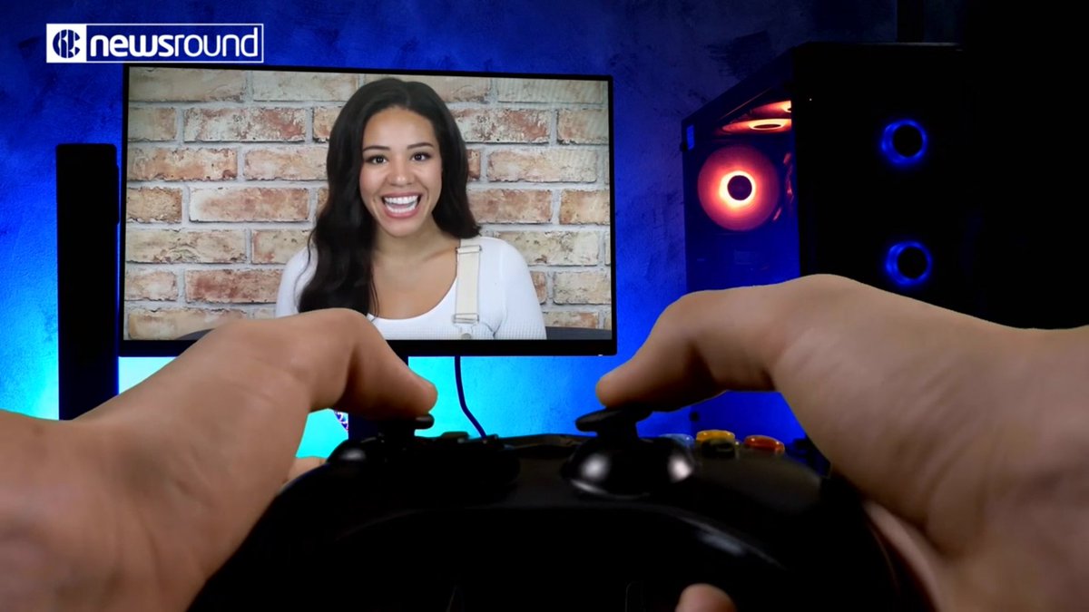 A still from a BBC Newsround report, showing Elle Osili-Wood, a mixed race woman with long dark hair, on a screen, while someone plays on an Xbox controller in the foreground.
